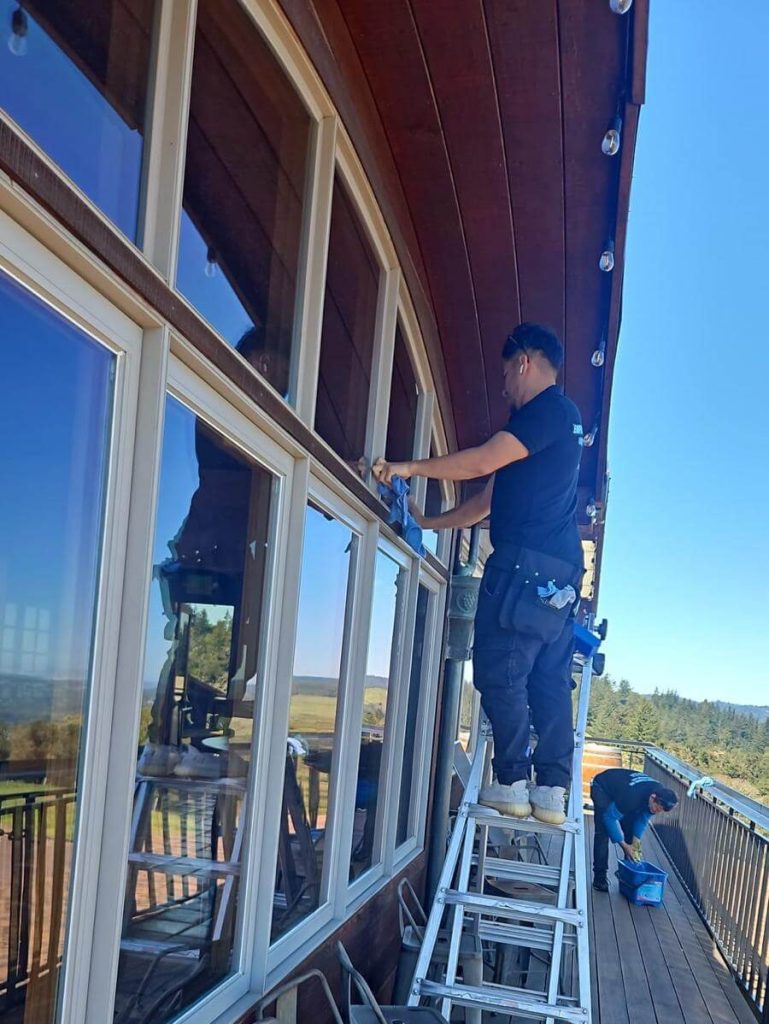 A window cleaner on a ladder wipes the window ledge on the upper windows of a building exterior