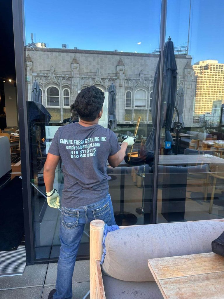 A window cleaner with a squeegee in front of a sparkling window that is reflecting a historic building in San Francisco