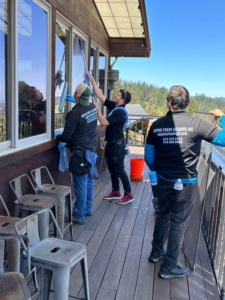 A team of window cleaners cleaning windows of a building on a deck overlooking the forest