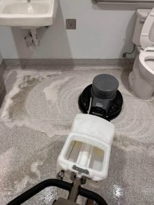 Bathroom floor being scrubbed with a brushing machine